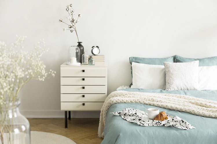 A bright bedroom interior with sage green and white bedding, pil