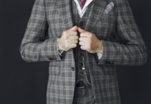 Close-up of a man adjusting a grey plaid three-piece suit featuring a pocket watch chain and maroon tie.